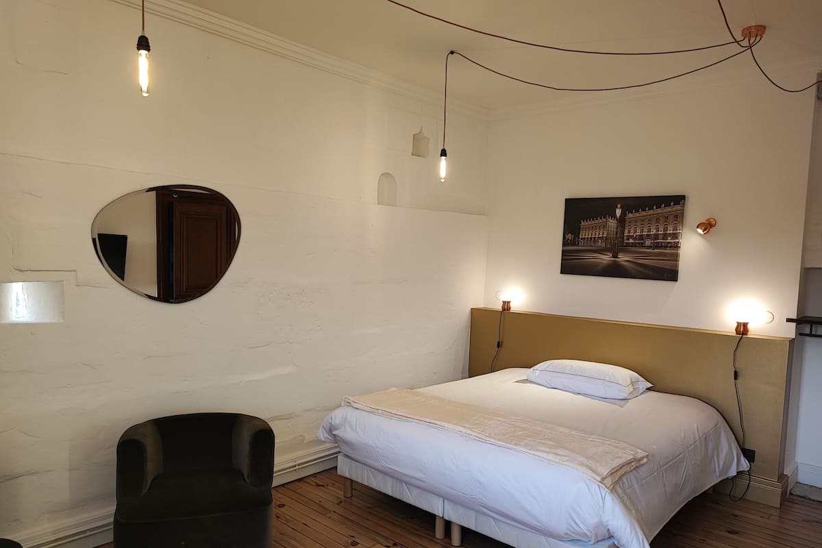 A bedroom with a bed, a chair, a mirror, and a wall-mounted picture.