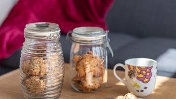 Two glass jars with contents on a wooden table, a mug with a colorful design, and a red cushion in the background.