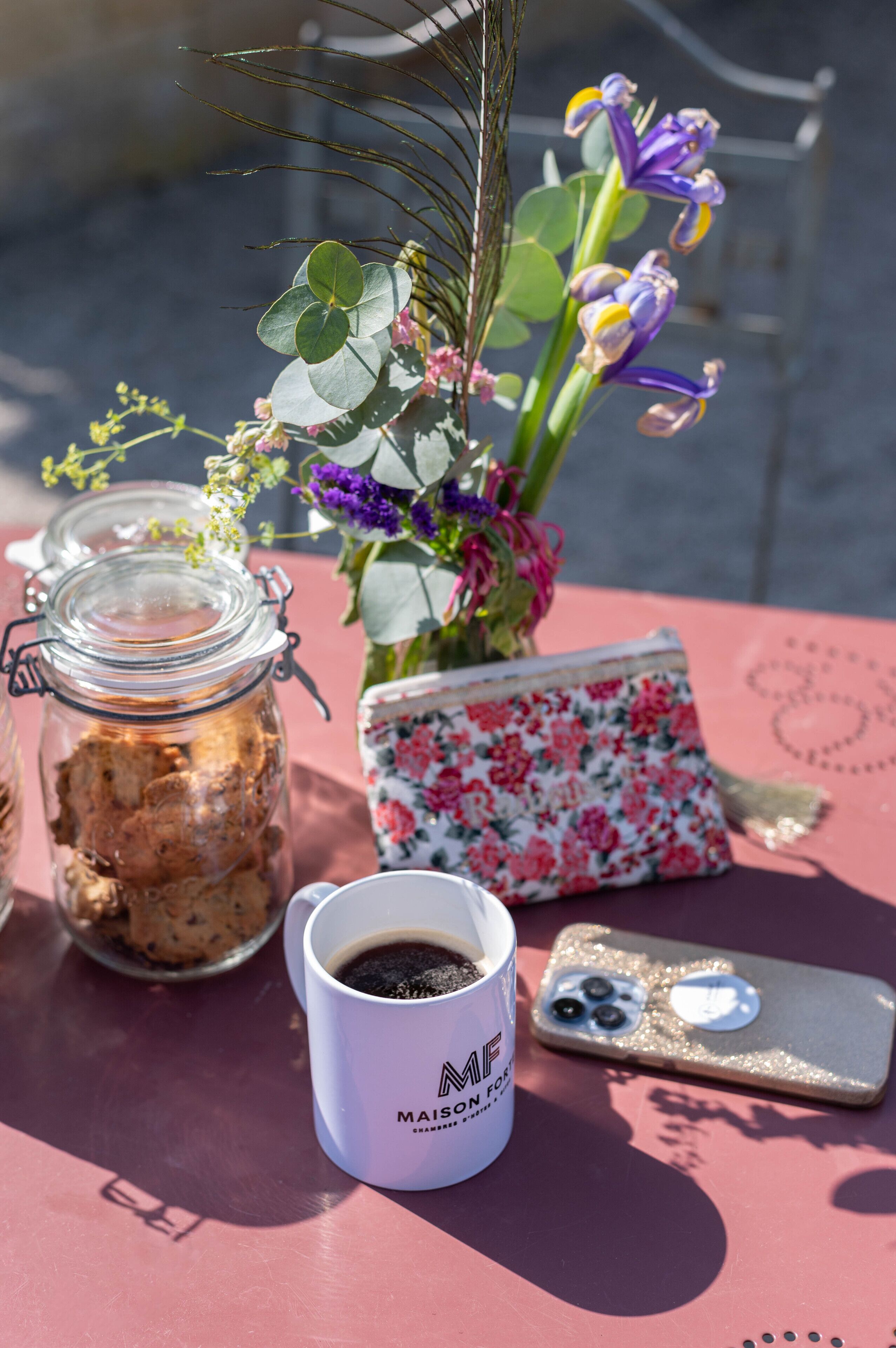 Une table avec une tasse de café, un téléphone, un bocal de biscuits et un arrangement floral.