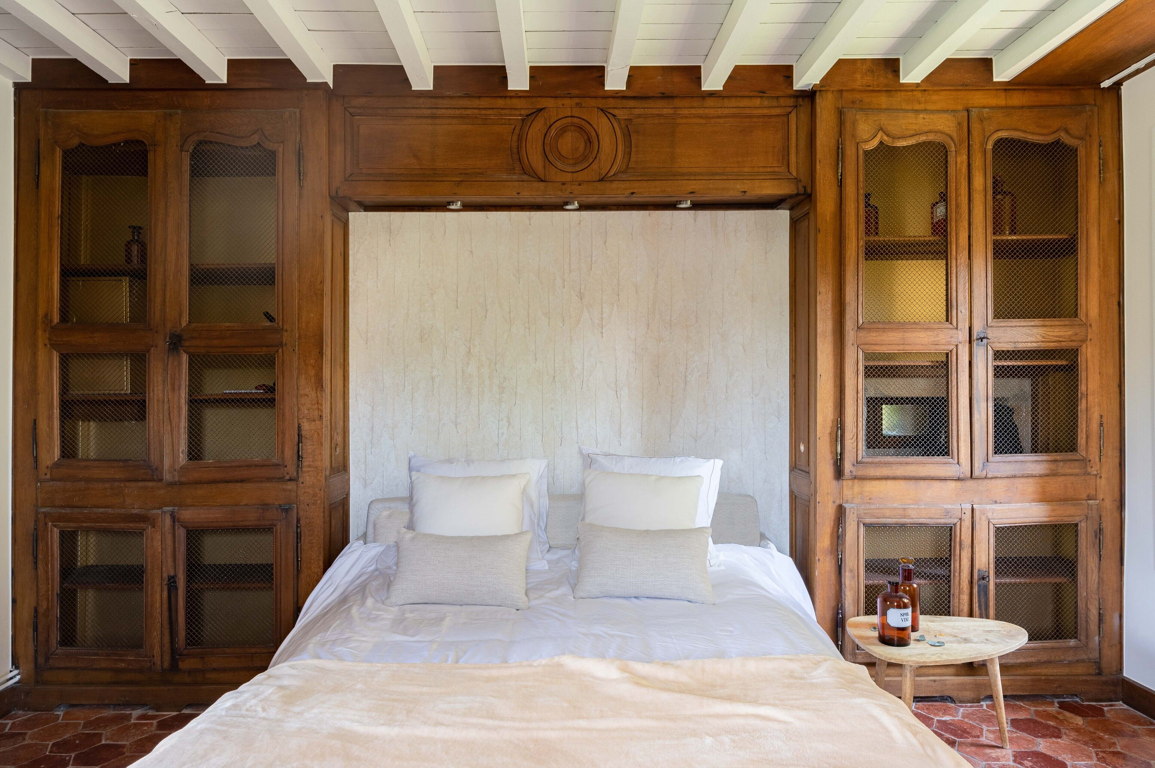 A bedroom with a large bed, wooden cabinets, and a small table with a bottle.
