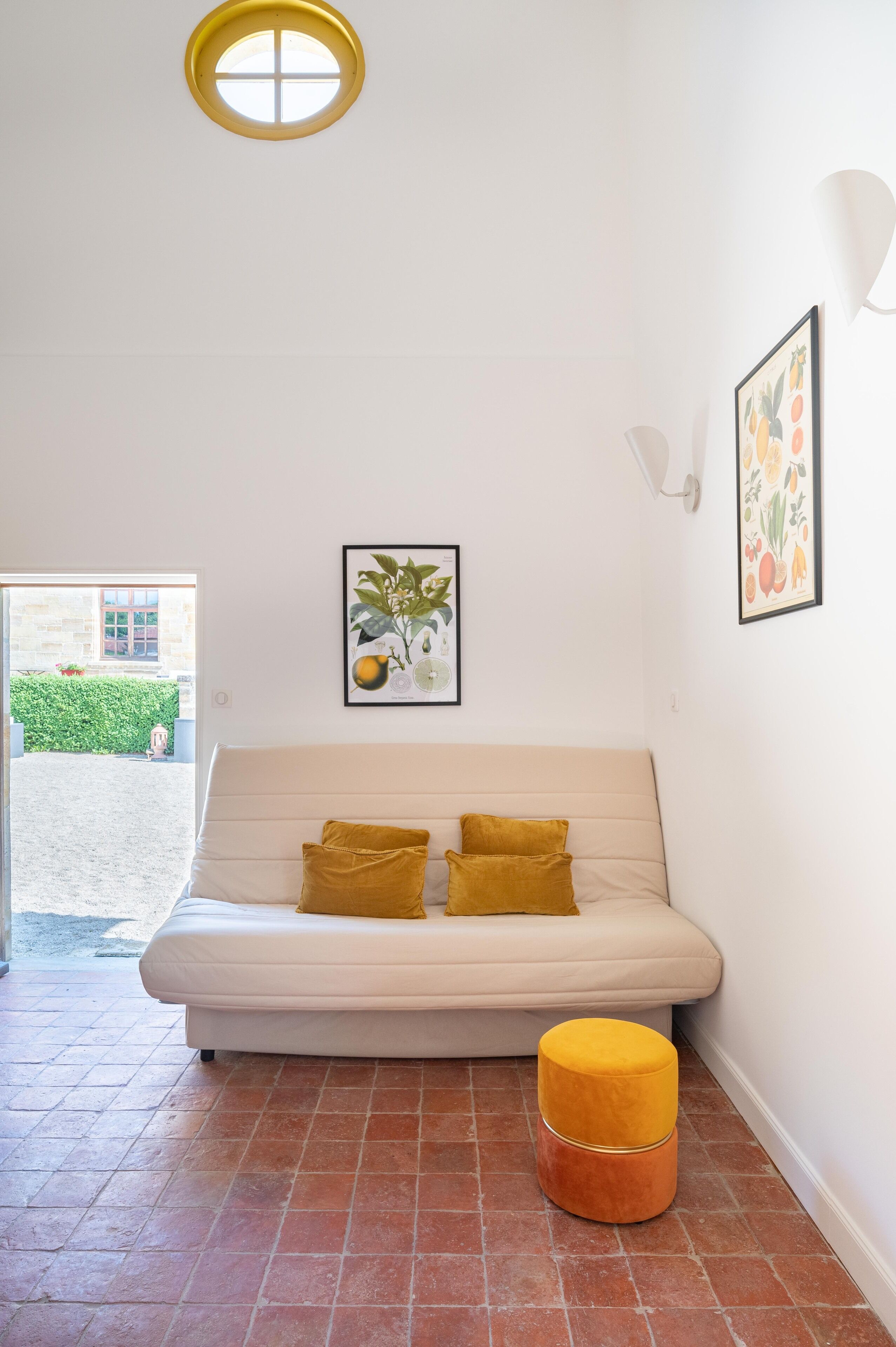 A white sofa with two mustard pillows, a yellow ottoman, and two framed botanical prints on the wall.
