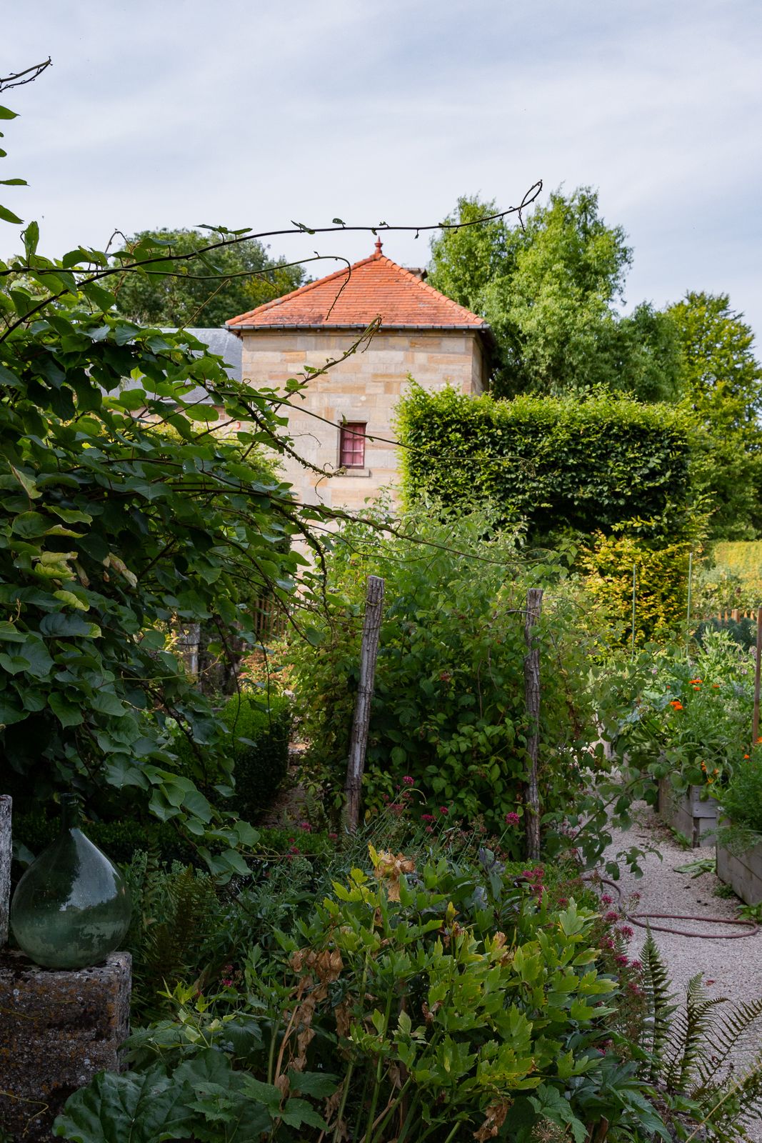 A stone building with a red-tiled roof, surrounded by lush greenery and a garden.