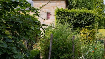 A stone building with a red-tiled roof, surrounded by lush greenery and a garden.