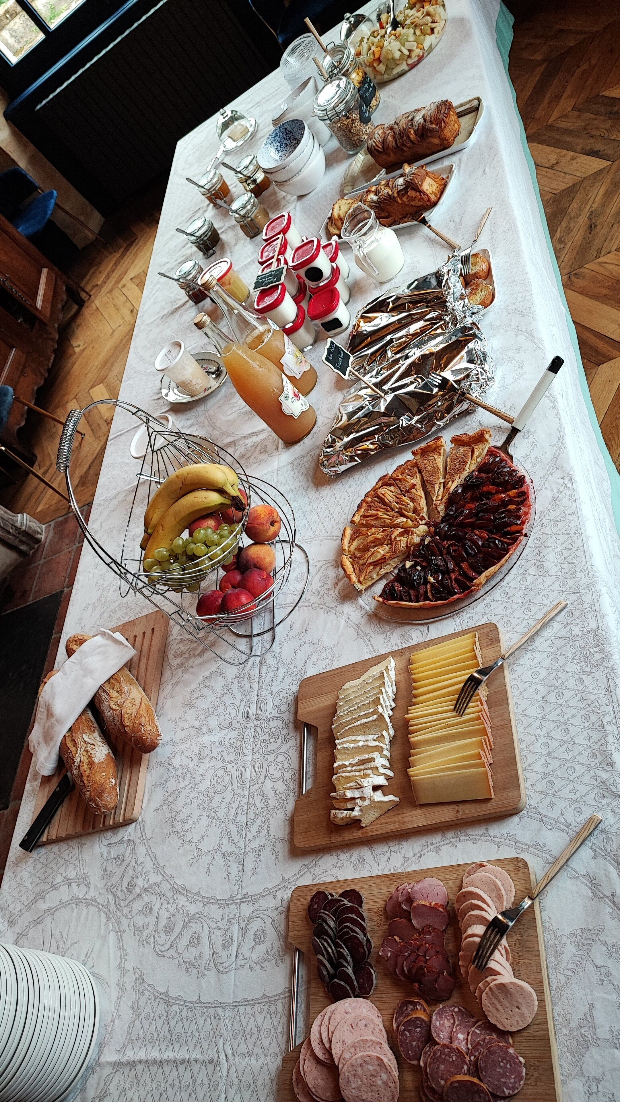 Une table sur laquelle sont disposés divers aliments, notamment des fruits, des fromages et des viandes, le tout présenté sur une nappe à motifs.