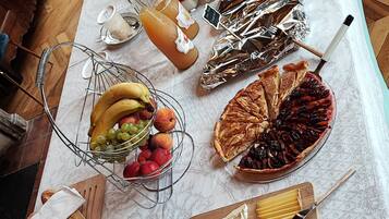 Une table sur laquelle sont disposés divers aliments, notamment des fruits, des fromages et des viandes, le tout présenté sur une nappe à motifs.