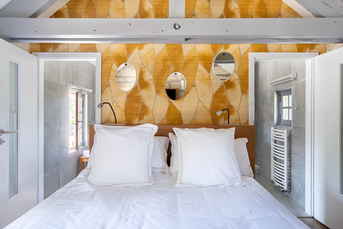 A bedroom with a bed, white bedding, a wooden headboard, and a patterned wall.