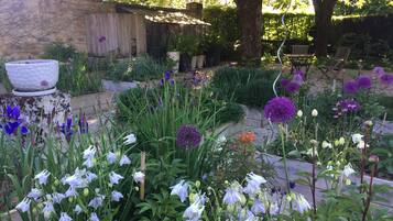 Un jardin agrémenté de diverses fleurs et plantes, un banc en bois et un bâtiment rustique doté d’un toit en pente.