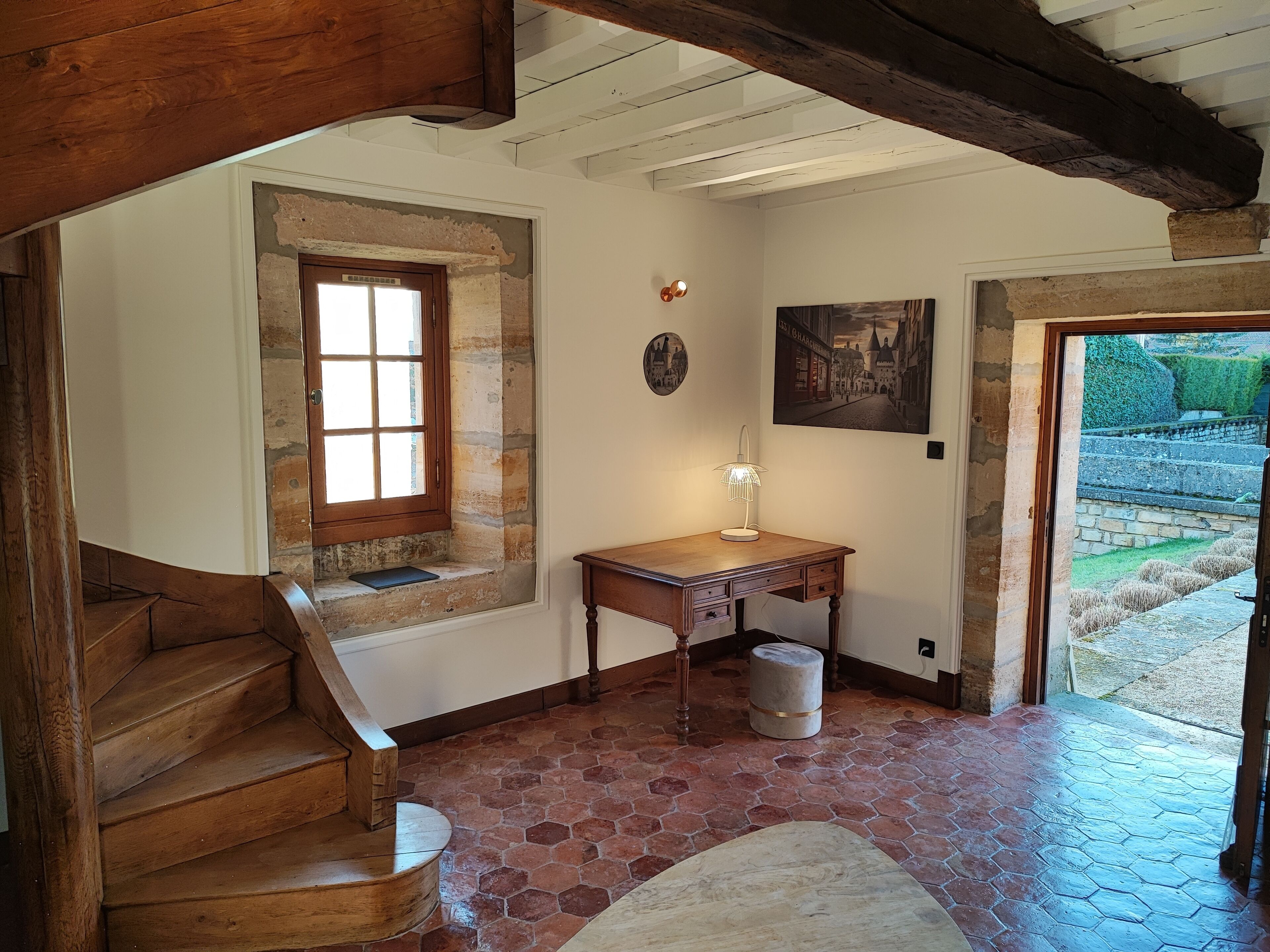 Una scala in legno conduce a una stanza con una parete in pietra, una scrivania in legno e un quadro.