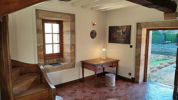 Una scala in legno conduce a una stanza con una parete in pietra, una scrivania in legno e un quadro.