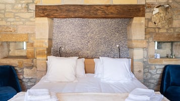 A neatly made bed with white linens and pillows, set against a stone wall with a wooden headboard.