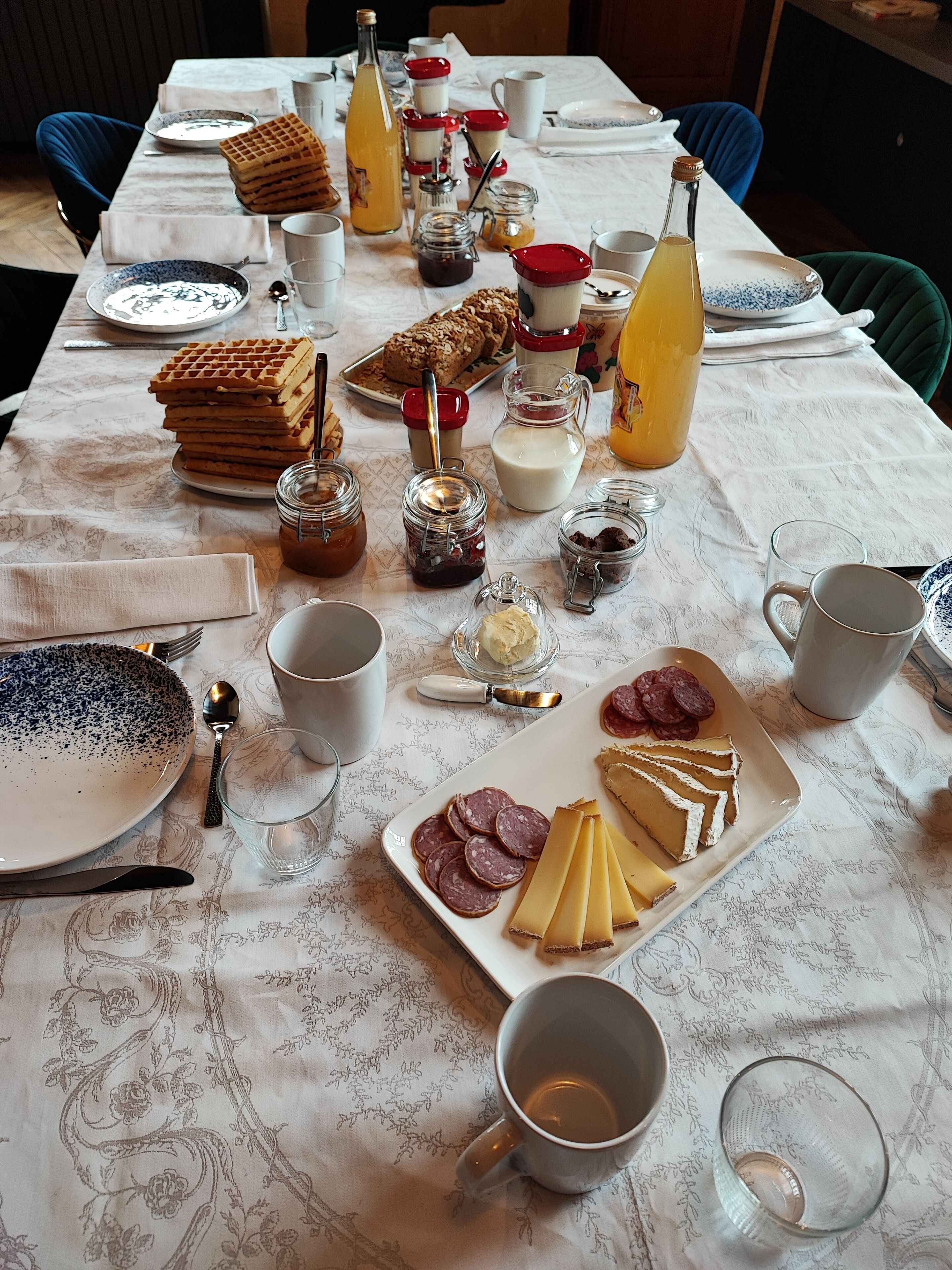 Una mesa de desayuno con waffles, pasteles, mermeladas, leche y queso.