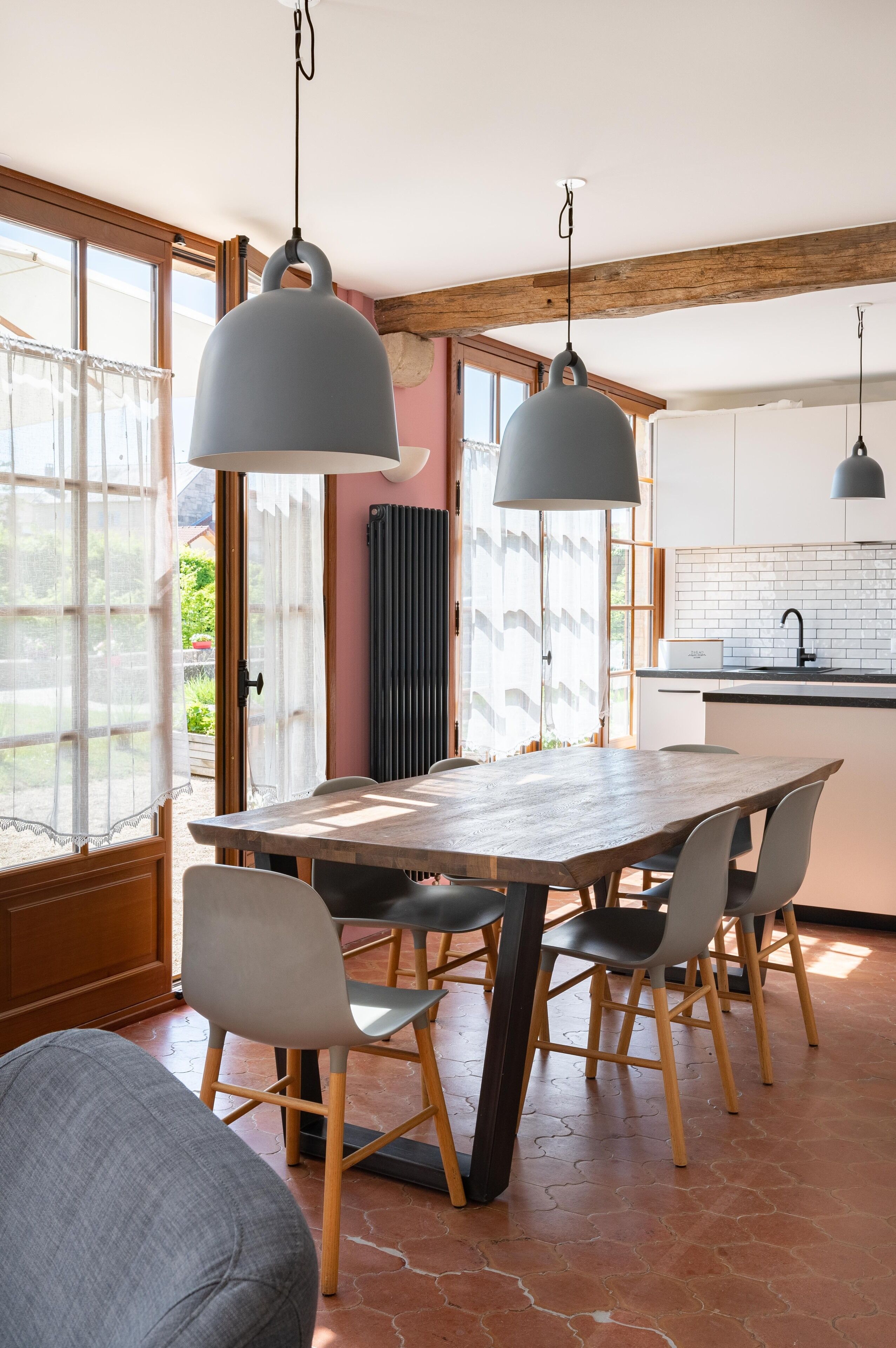 A dining area with a wooden table and chairs, pendant lights, and a view of the outdoors through large windows.