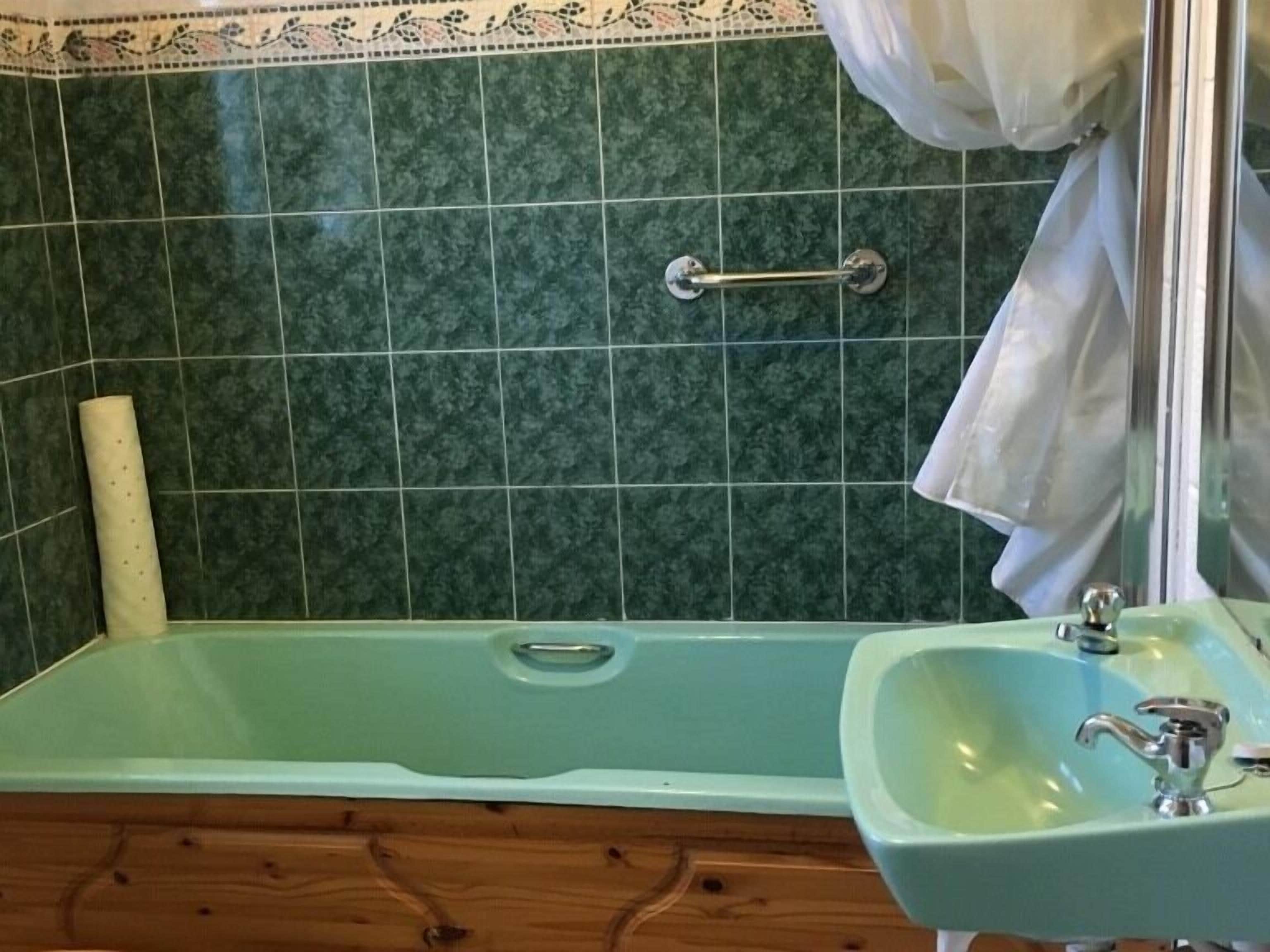 Une salle de bain avec un mur recouvert de carreaux verts, une baignoire et un lavabo avec un miroir.