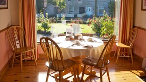 A dining area with a round table set for four, wooden chairs, and a view of a garden through a large window. - Ach na Sheen Guest House (Tipperary)