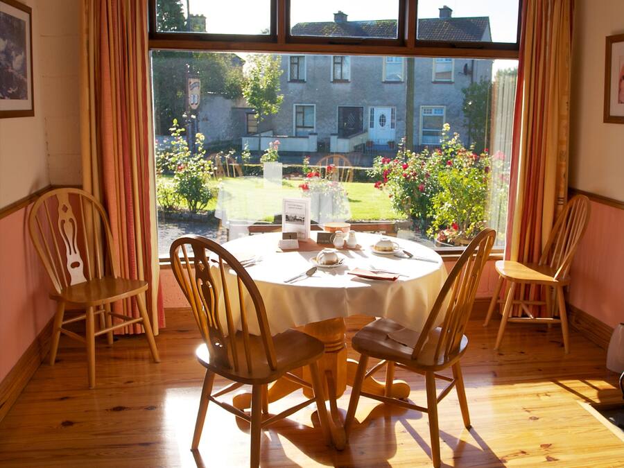 Un comedor con una mesa redonda para cuatro personas, sillas de madera y vistas a un jardín a través de un ventanal amplio.
