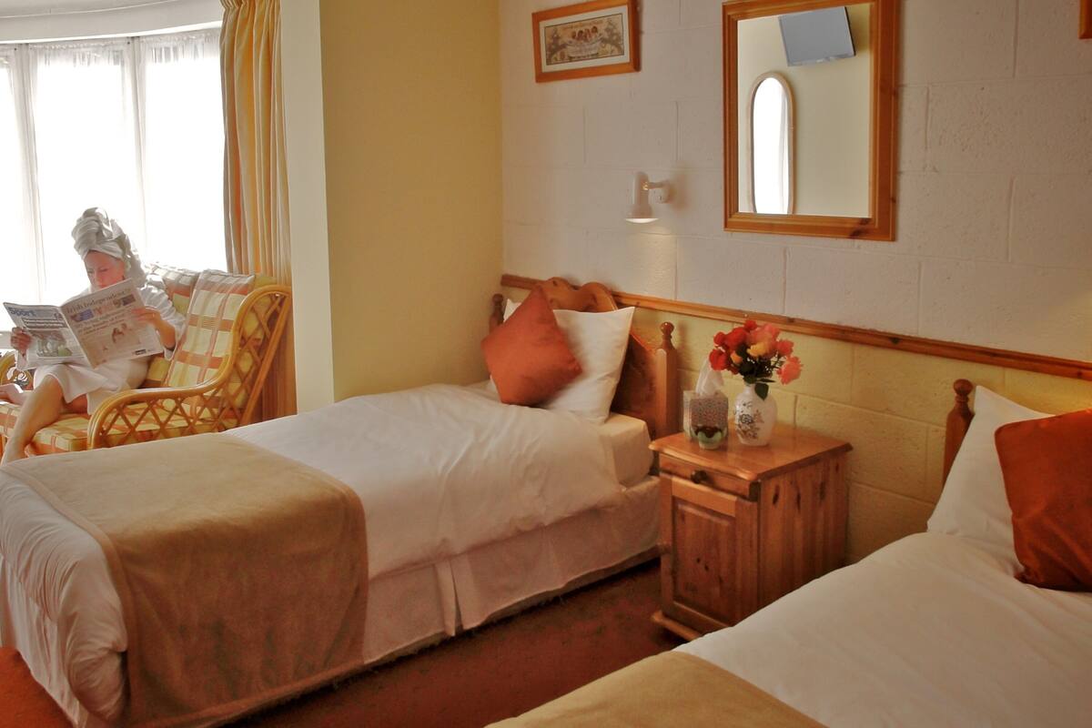 Une chambre d’hôtel avec deux lits, une table de chevet en bois, un miroir et une fenêtre avec des rideaux.