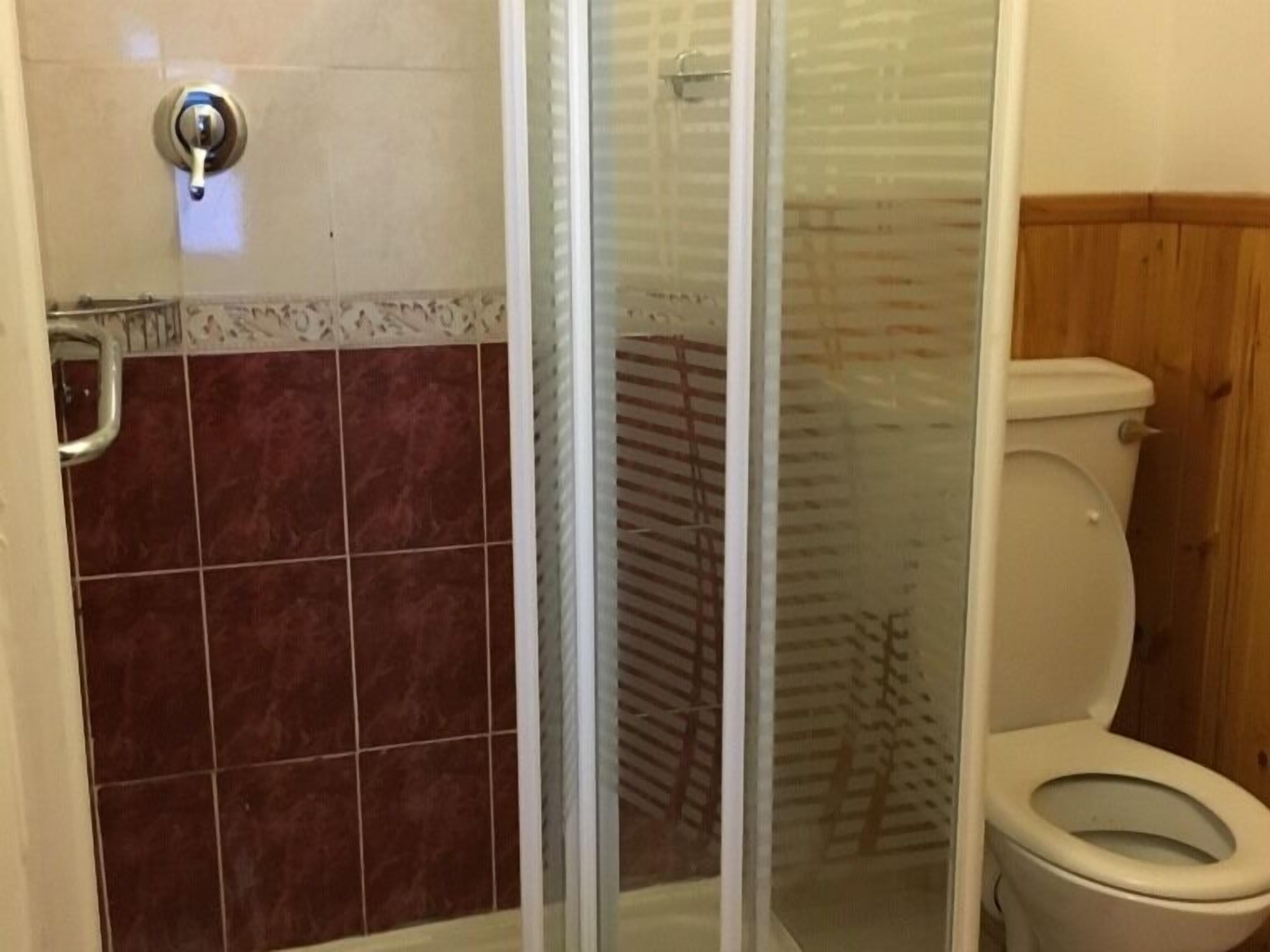 A bathroom with a glass shower enclosure, a toilet, and tiled walls.