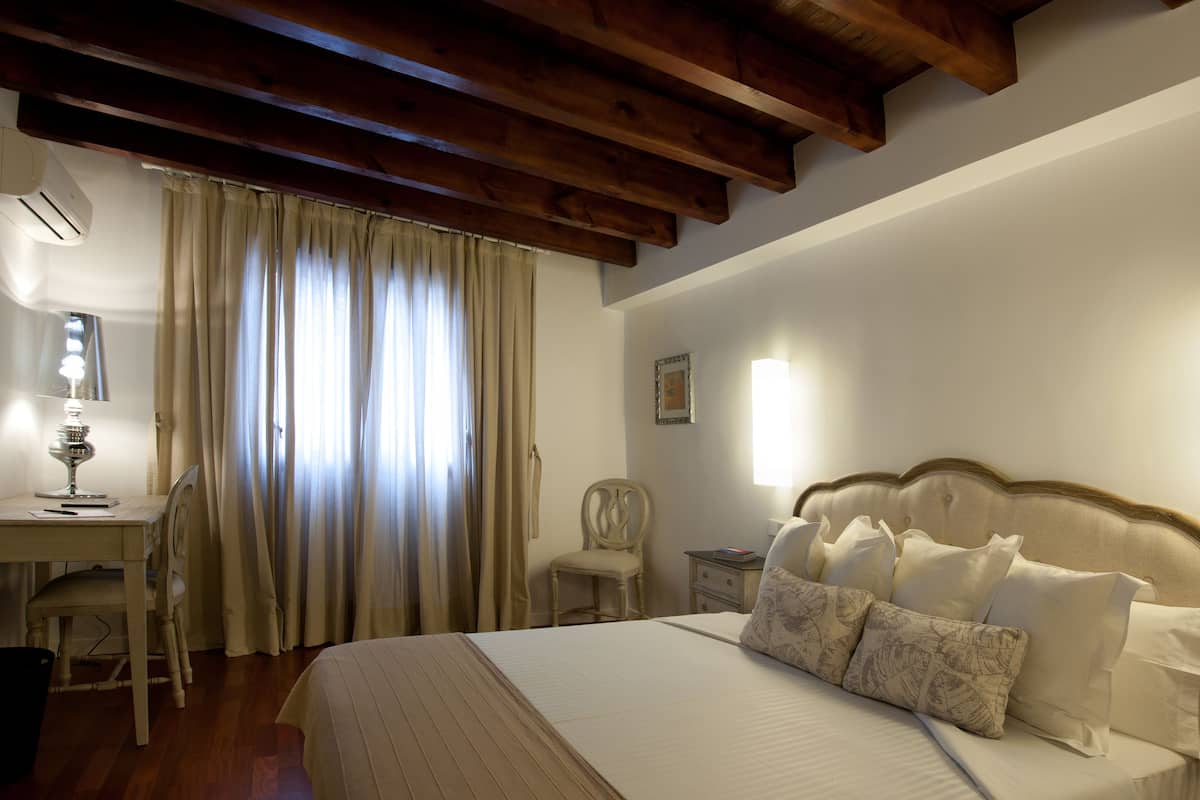 A bedroom with a large bed, a desk with a lamp, and a chair.