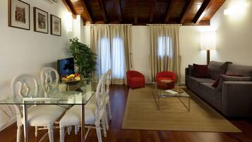 A modern living room with a glass dining table, white chairs, a red armchair, a grey sofa, and a wooden ceiling.