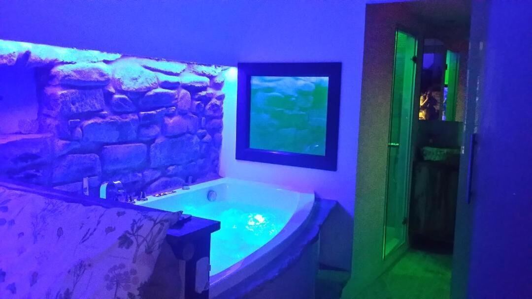 Une pièce avec un mur en pierre, un tableau encadré, une baignoire et une porte dotée d’un panneau de verre.
