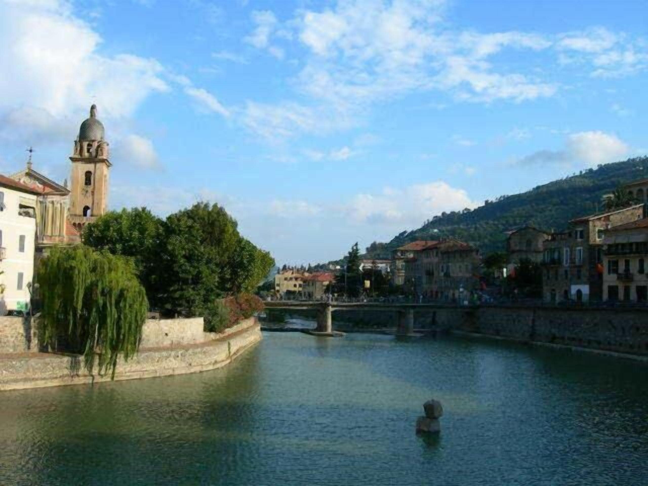 Een historische stad met een rivier, een brug en een opvallende kerktoren.
