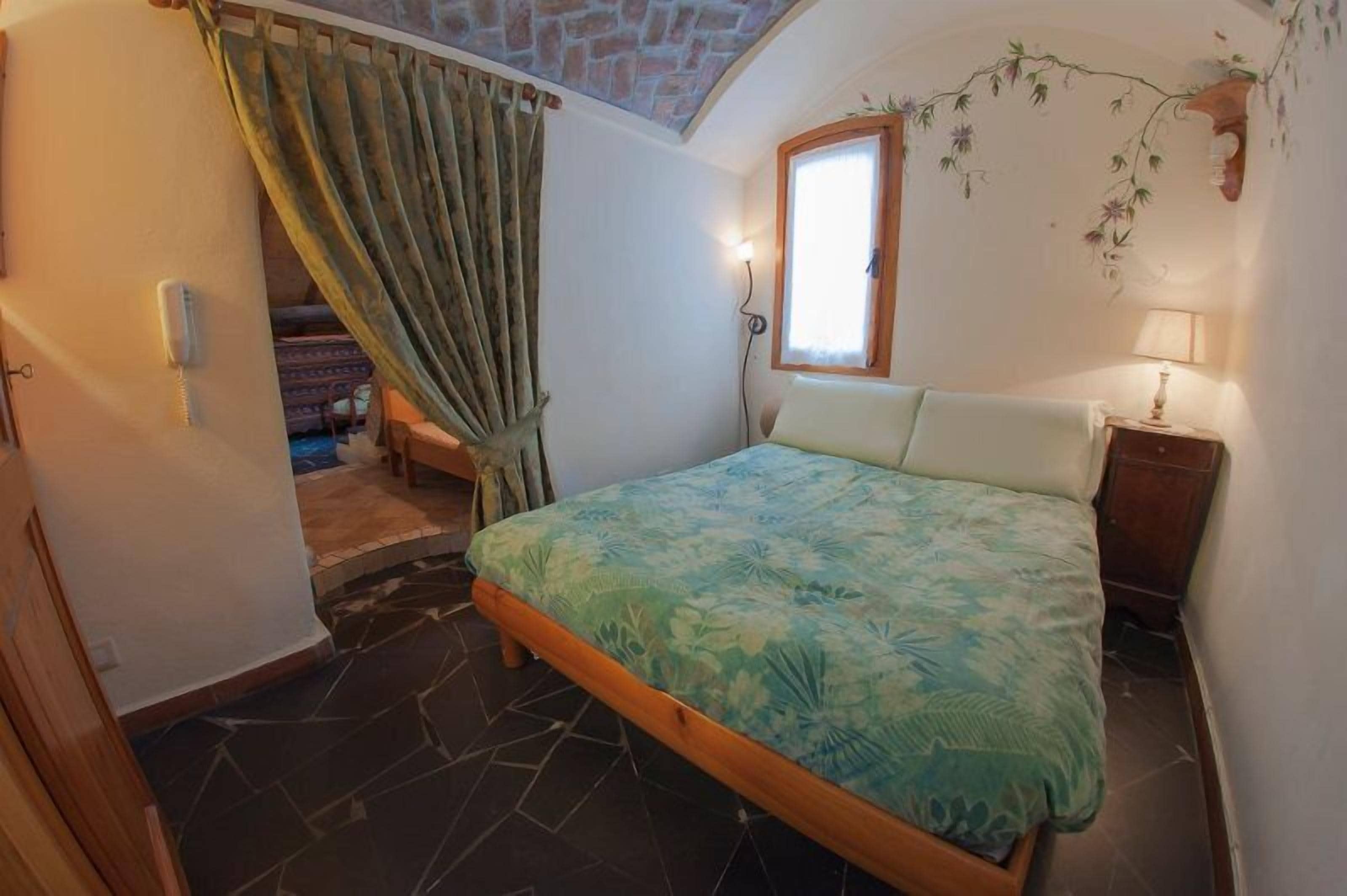 A bedroom with a bed, a window, a lamp, and a curtain.