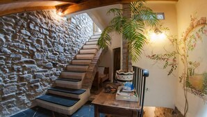 Een stenen trap die leidt naar een houten plafond, een tafel met een plant erop, en een muur met bloemistisch kunstwerk.