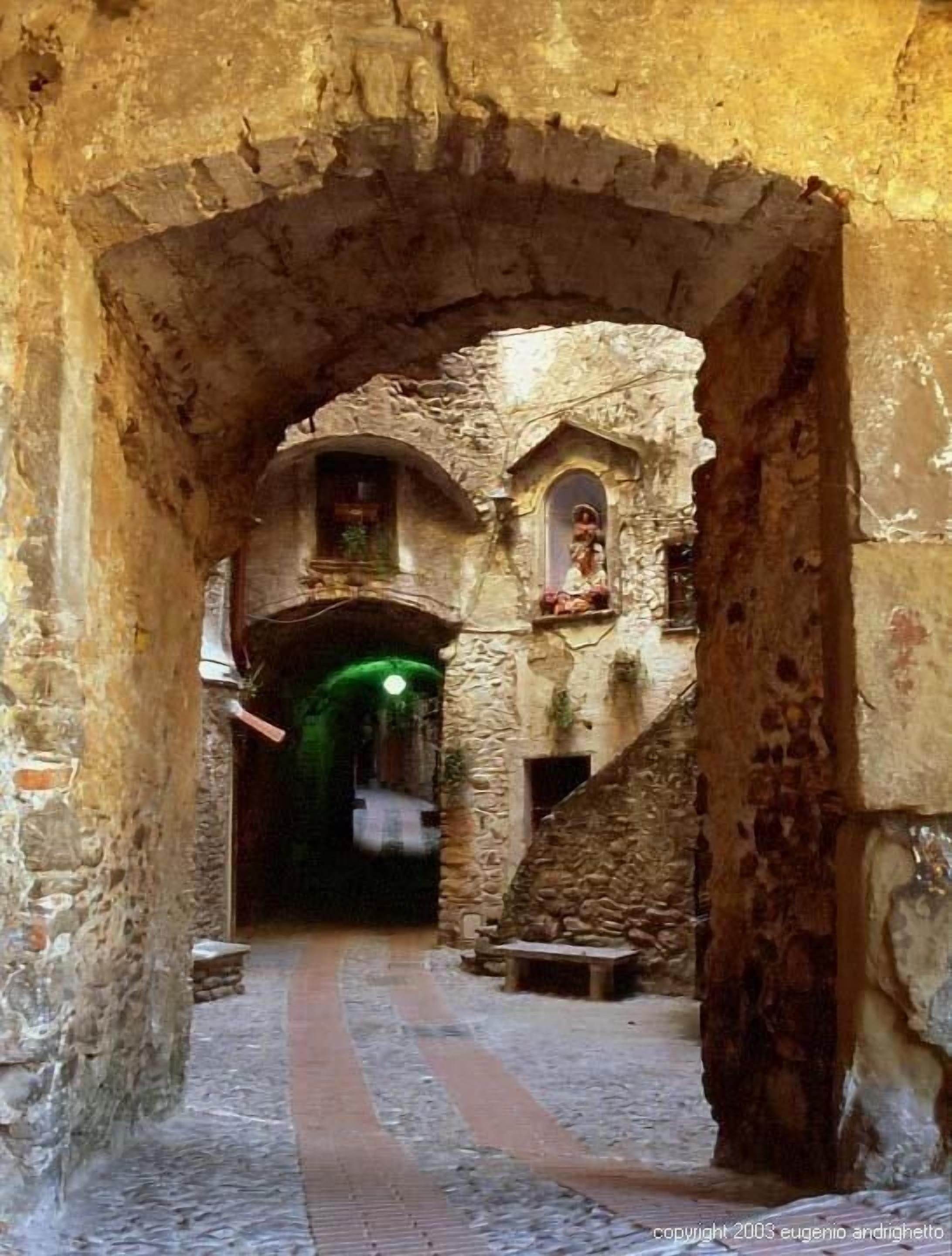 An ancient stone archway leading to a narrow passageway with a stone bench and a small shrine.