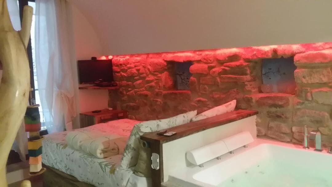 Un dormitorio con pared de piedra, cama con ropa de cama floral, televisor y bañera.