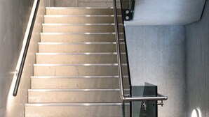Een trap met metalen leuningen en een glazen deuropening voor een lift.
