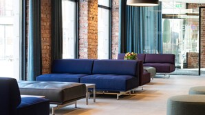 Een moderne lobby met een blauwe bank, een grijze poef en een paarse fauteuil.