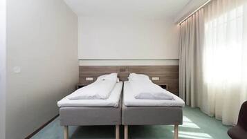 A hotel room with two single beds, a wooden headboard, a light-colored floor, and a window with curtains.