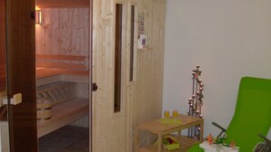 A sauna room with a wooden bench, a small table with drinks, and a green chair. - Hotel Müritzperle (Waren (Müritz))