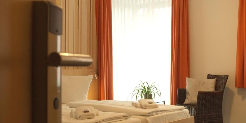 Una habitación de hotel con cama, una silla, una planta en maceta y una ventana con cortinas.
