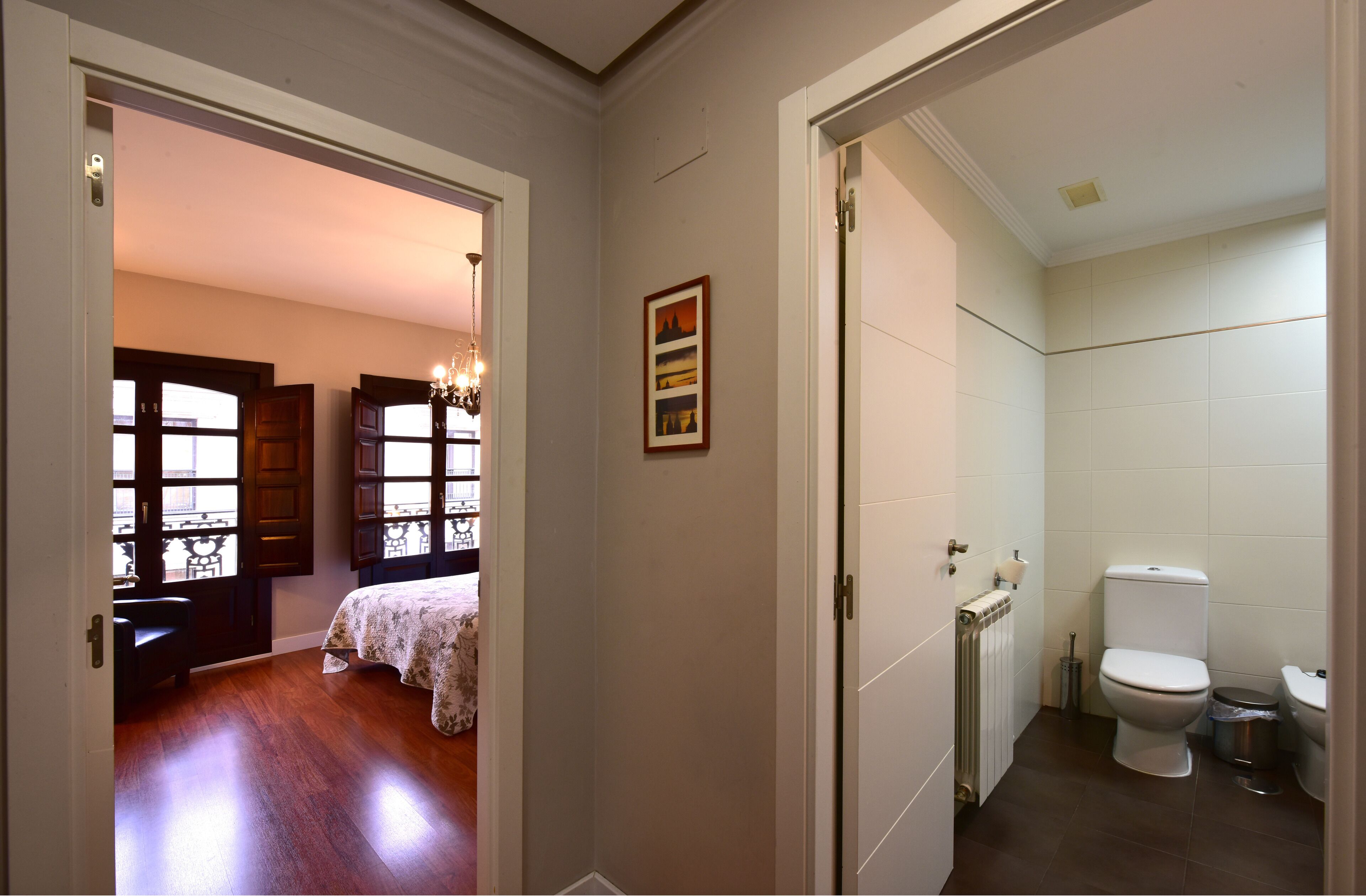 A bedroom with a bed, a bathroom with a toilet, and a hallway with a door leading to another room.