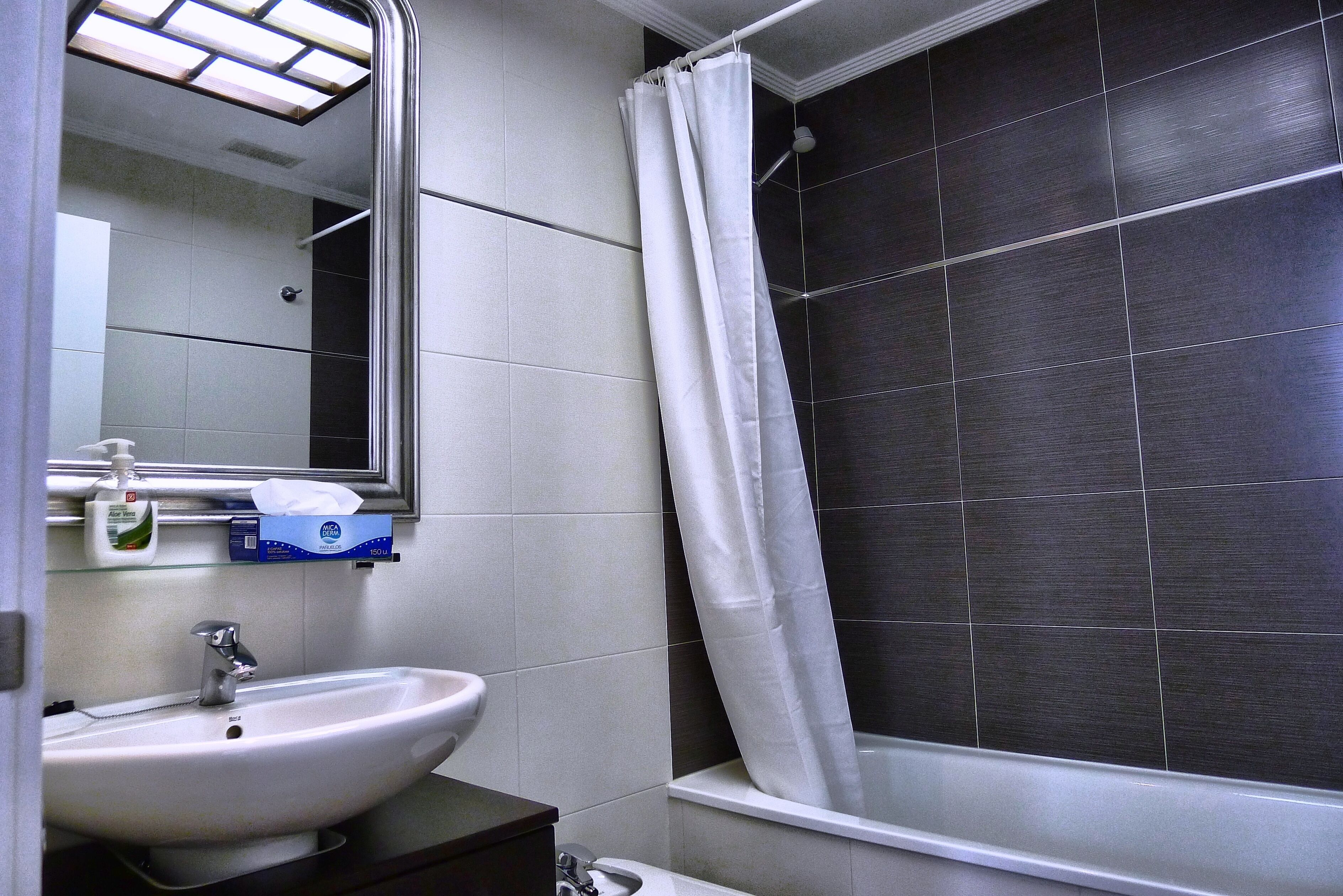A bathroom with a white sink, a mirror, a shower curtain, and dark tiled walls.