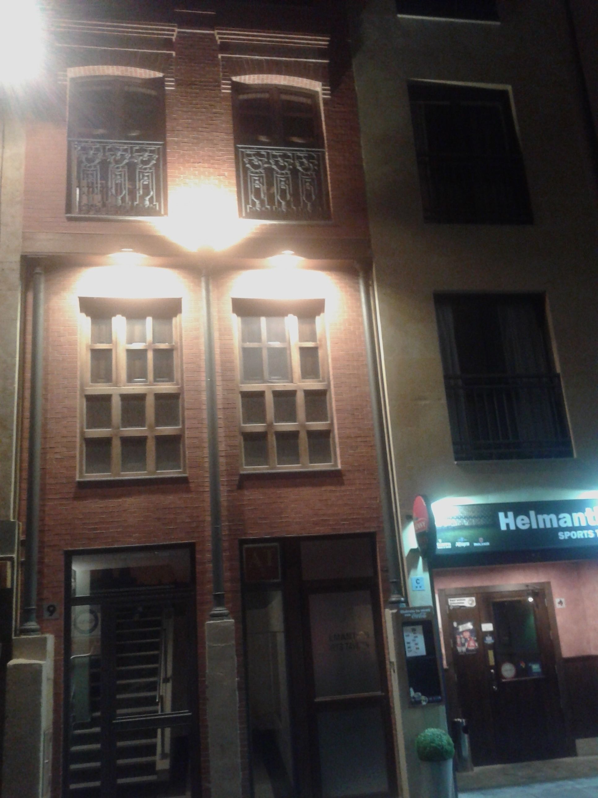 Un edificio con dos ventanas iluminadas y un letrero que dice 'Helmant Sports'.