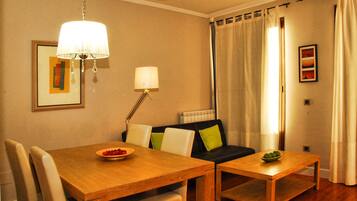 Un comedor con una mesa y sillas de madera, una mesita auxiliar con un cuenco, un sofá con cojines, una lámpara de pie y un cuadro enmarcado en la pared.
