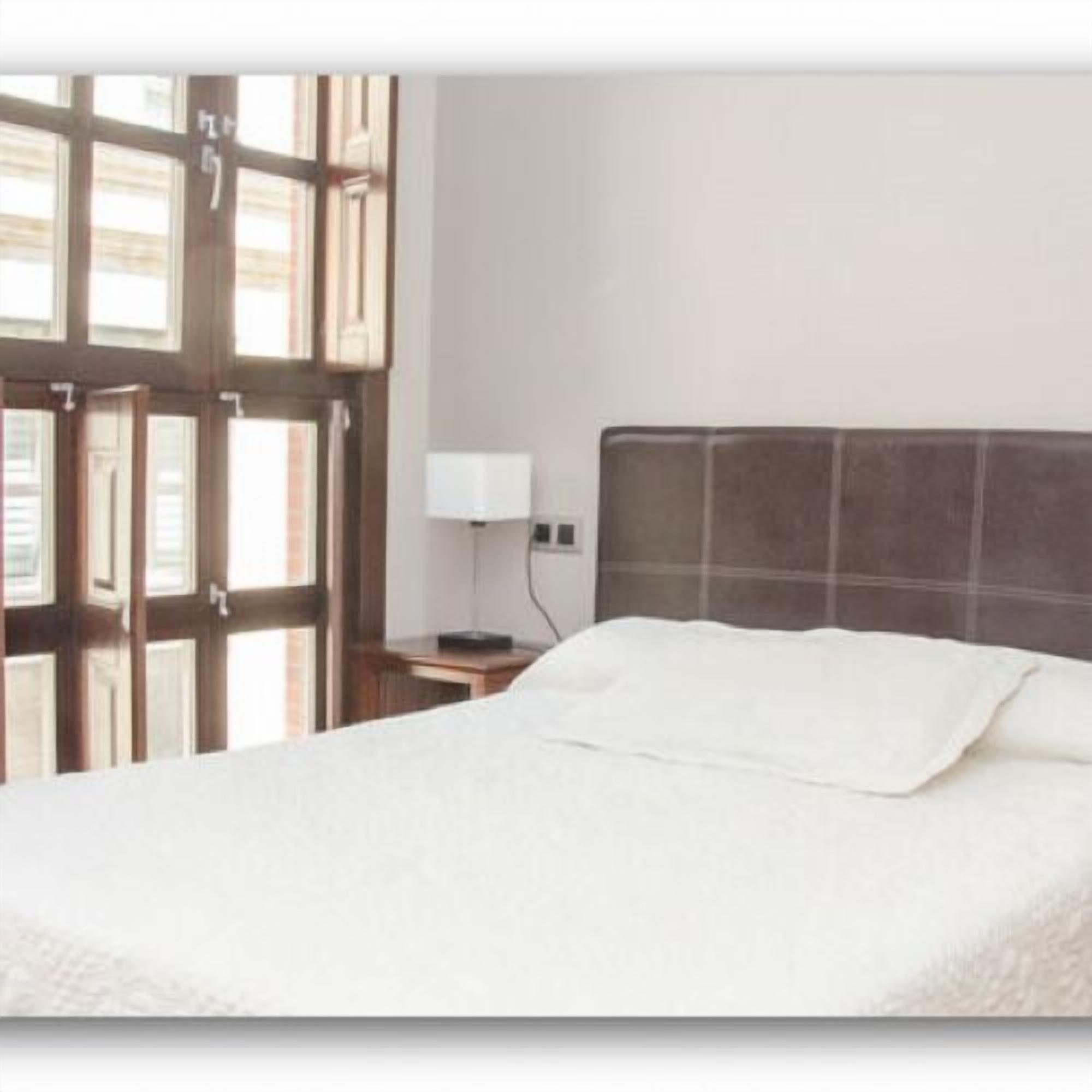 Une chambre d’hôtel avec un grand lit, une table de chevet avec une lampe et une fenêtre avec des stores.