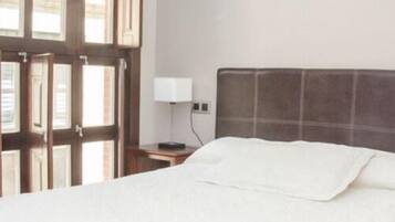 Une chambre d’hôtel avec un grand lit, une table de chevet avec une lampe et une fenêtre avec des stores.