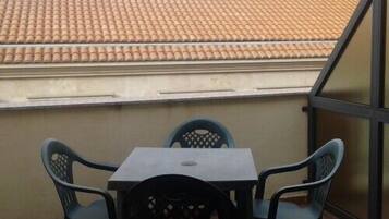Un pequeño balcón con techo de tejas, una mesa y cuatro sillas.