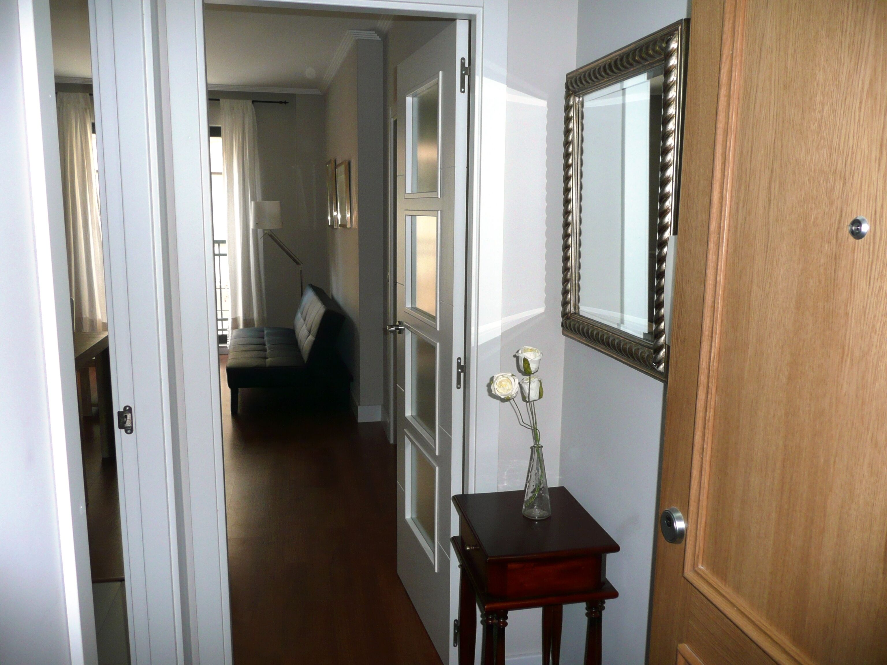 Un couloir avec une porte en bois, un miroir et une petite table sur laquelle est posé un vase.
