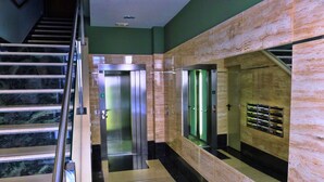 Een moderne lift met een metalen afwerking, een marmeren wand en een glaspaneel met een groen licht.