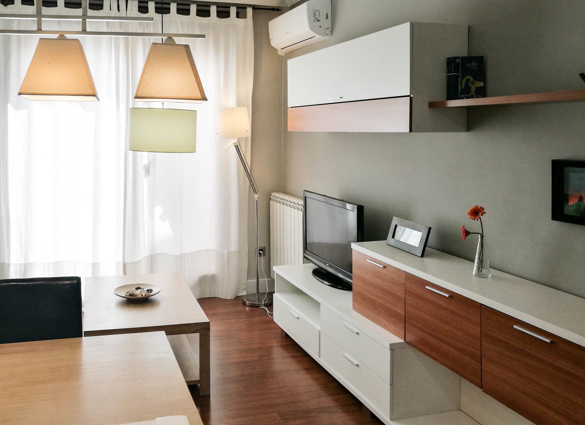 Ein modernes Hotelzimmer mit Essbereich, Flachbildfernseher, kleines Schränkchen und Heizkörper.
