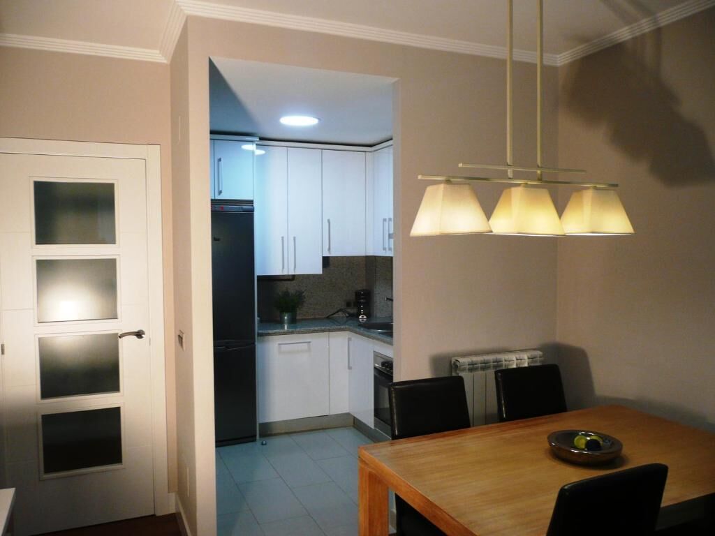 Una cocina compacta con armarios blancos, un refrigerador y un comedor con mesa y sillas.