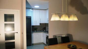 Una cocina compacta con armarios blancos, un refrigerador y un comedor con mesa y sillas.