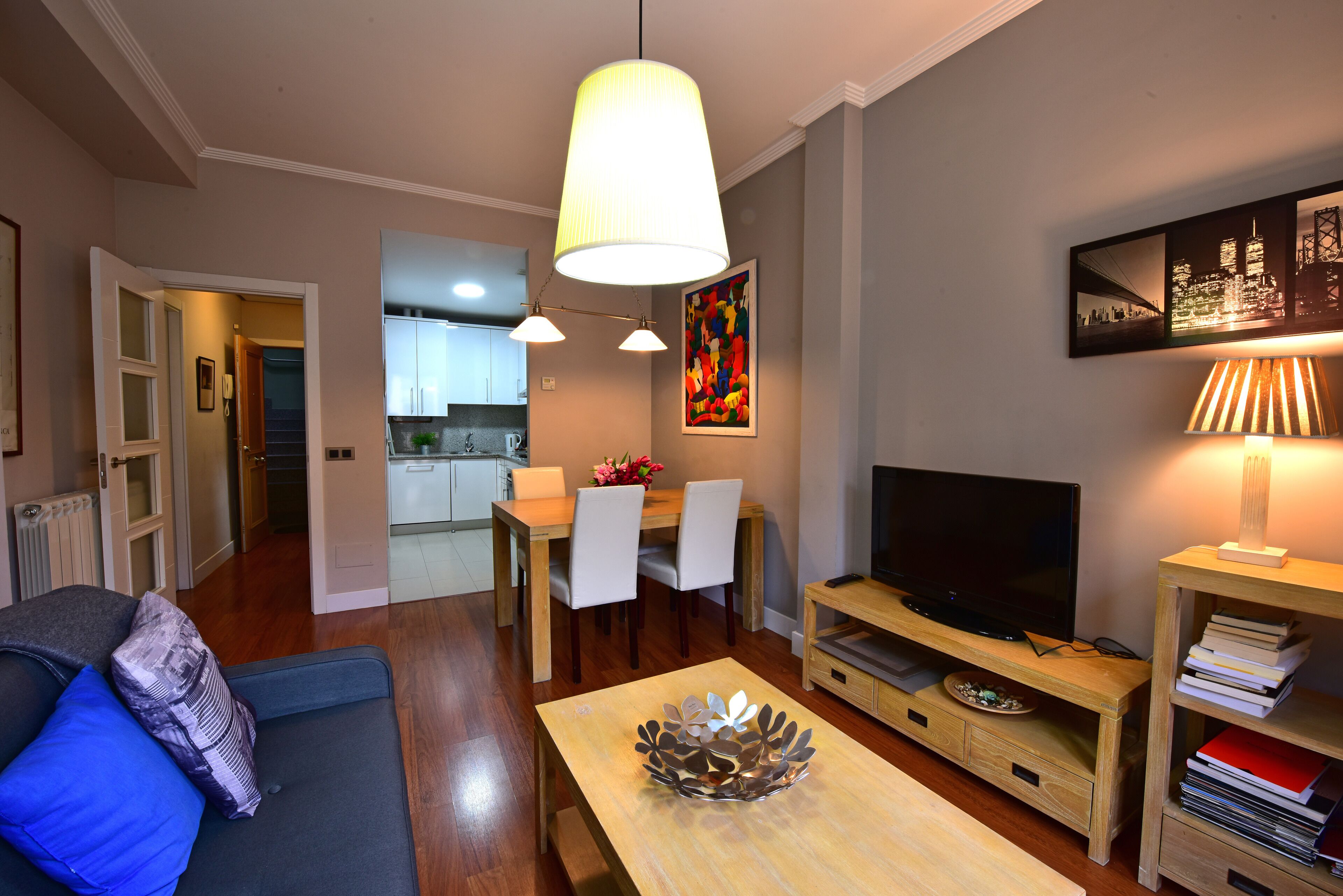 Una sala de estar moderna con sofá, mesa de centro, televisor y comedor con sillas y una mesa.