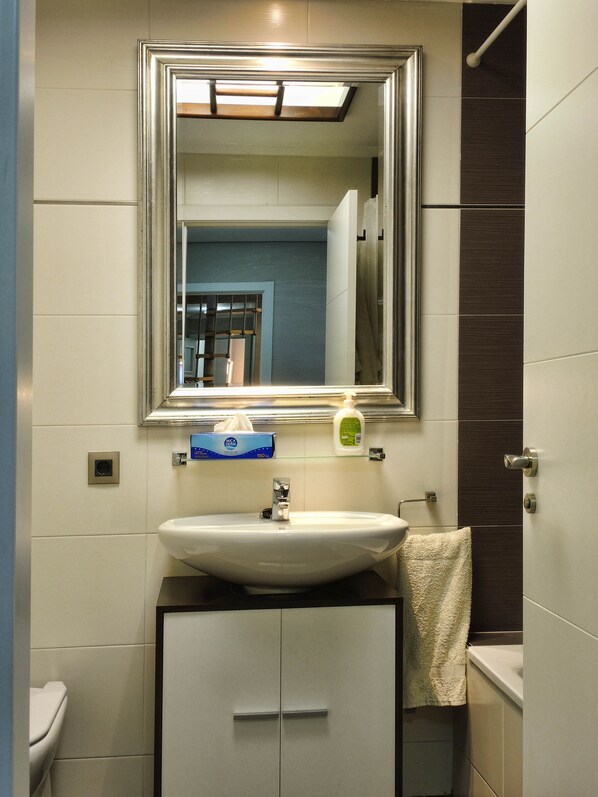 A bathroom with a white sink, a mirror above it, a towel hanging on the wall, and a toilet.