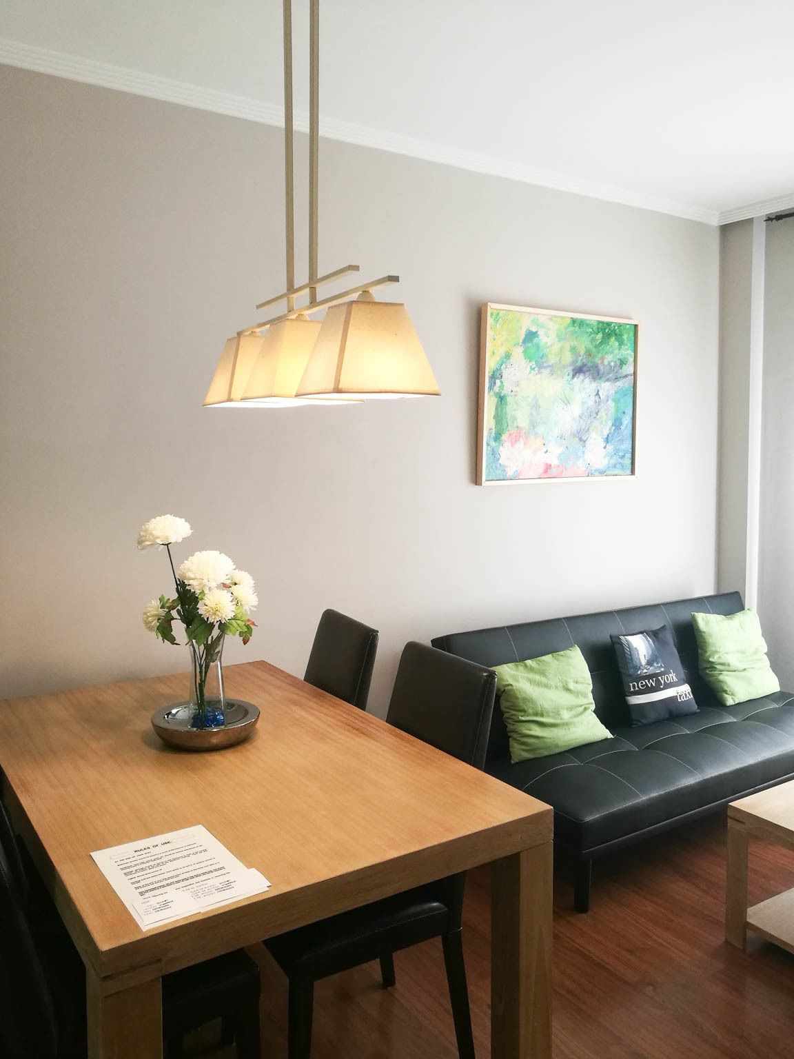 Una sala de estar moderna con una mesa de comedor de madera, un sofá de cuero negro y un cuadro abstracto colorido en la pared.