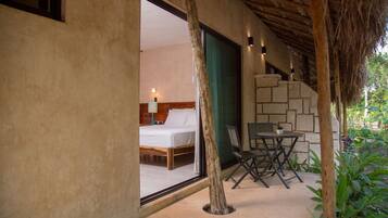 Un dormitorio con cama, mesita de noche y ventana. Hay una pequeña mesa y una silla fuera de la habitación.